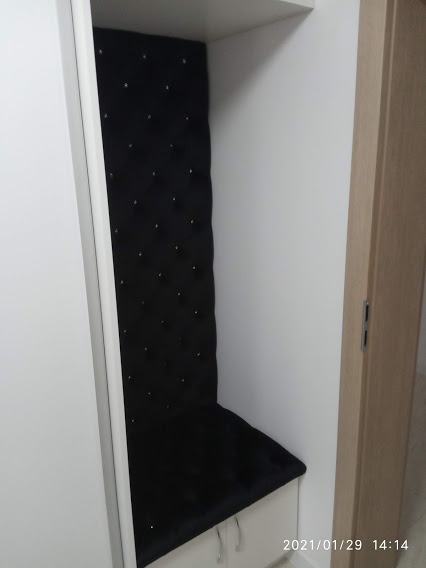 Wnęka z tapicerowanym, czarnym siedziskiem i oparciem z guzikami, wbudowana w białą szafę.