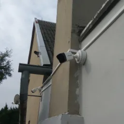 Zewnętrzny montaż kamer monitoringu Hikvision na elewacji budynku, widoczny rynna spustowa i fragment dachu.