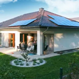 Dom jednorodzinny z panelami słonecznymi na dachu, widok z ogrodu z elementami architektury krajobrazu.