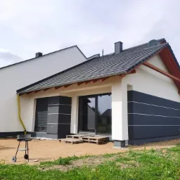 Wykończona elewacja domu jednorodzinnego w Zielonej Górze, z dwukolorową fasadą (biały i grafitowy), widoczne detale wykończeniowe i fragment ogrodu.