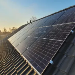 Panele słoneczne zamontowane na ciemnym, ceramicznym dachu w promieniach zachodzącego słońca, widok z góry.