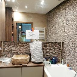 Ideal-bud Paweł Okhovych Firma remontowo-wykończeniowa - Umywalka z kamienia w łazience z mozaikową ścianą, torba w paski i kartka 'świeżo klejone podpórki, używać w niedzielę' przyklejona do lustra.