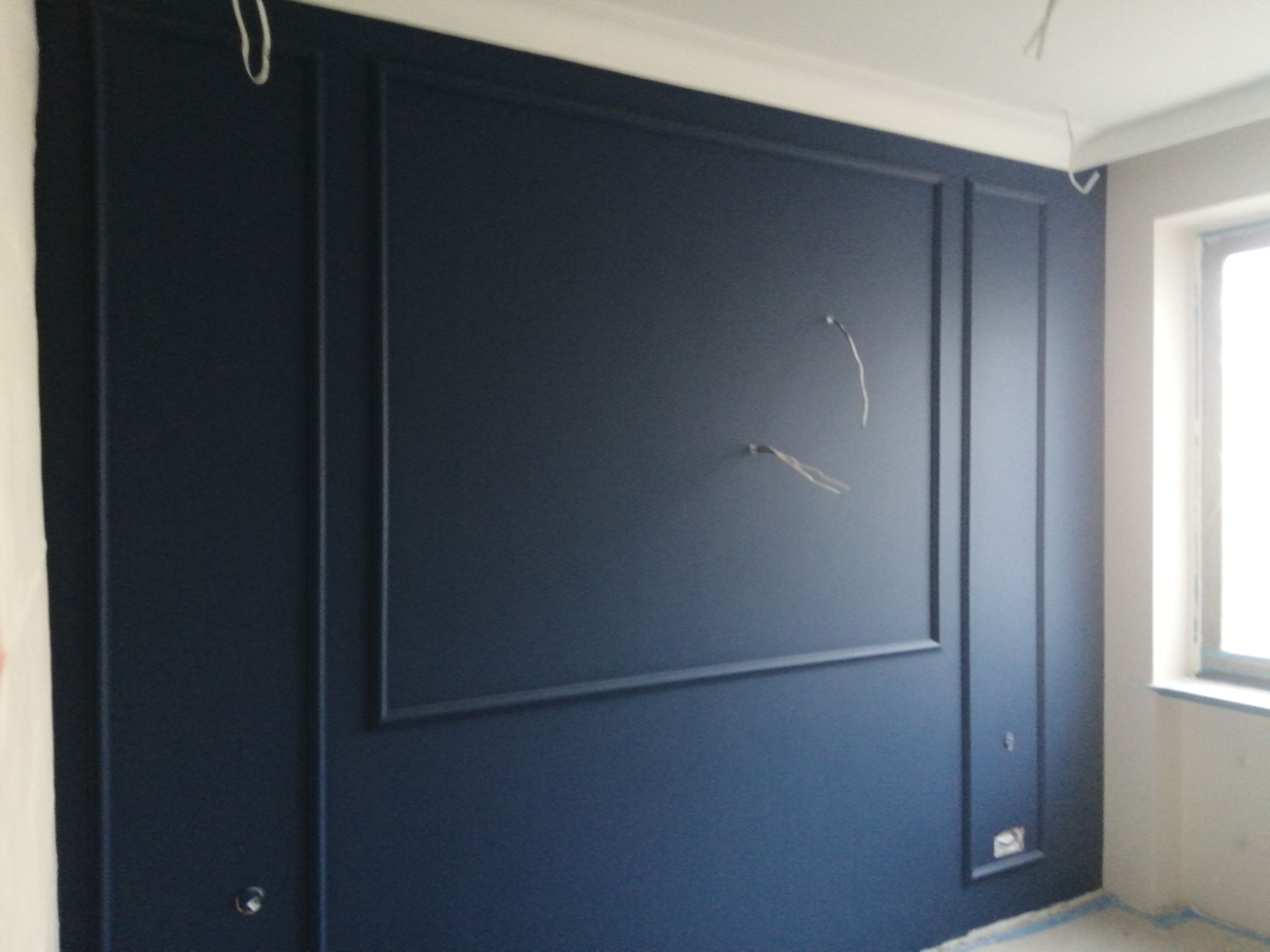 Ściana w kolorze granatowym z dekoracyjnymi panelami i listwami przysufitowymi, widoczne przewody elektryczne wystające ze ściany, przygotowana do montażu gniazdek.