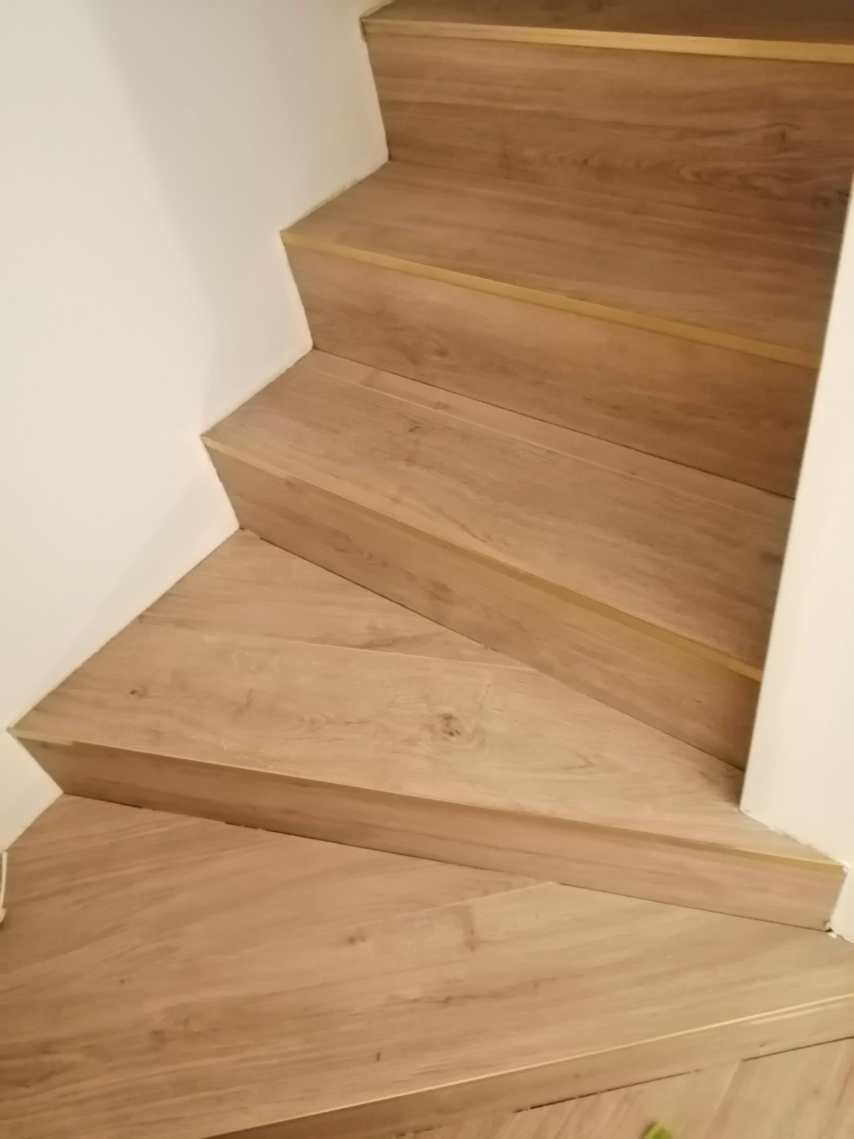Schody drewniane z jasnego parkietu, z widocznymi listwami przypodłogowymi i białymi ścianami, ujęcie z góry.