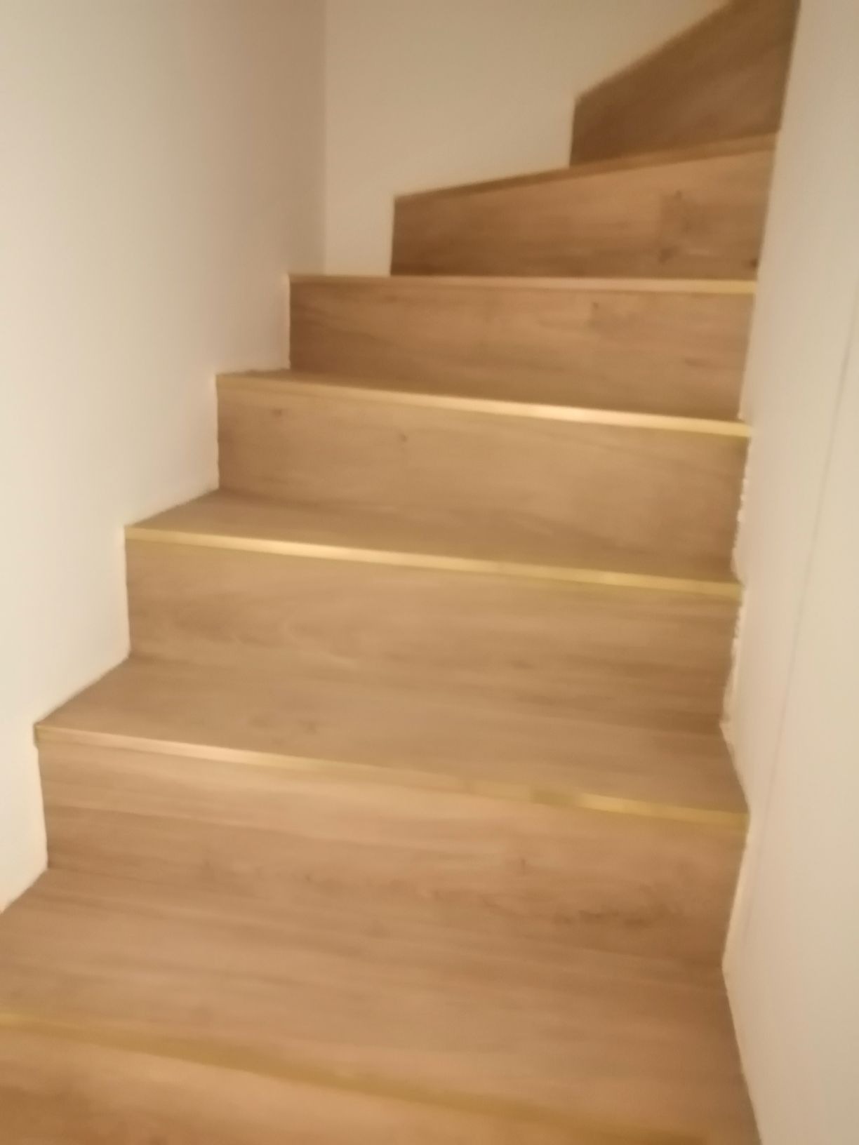 Schody wykończone panelami z drewnopodobnym wzorem i złotymi listwami krawędziowymi, widok z dołu.