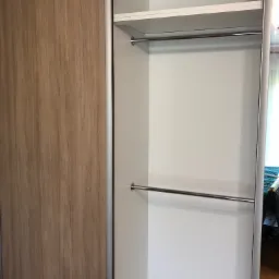 Wnętrze szafy wnękowej z przesuwnymi drzwiami w odcieniach drewna, widoczne półki i drążki na ubrania.