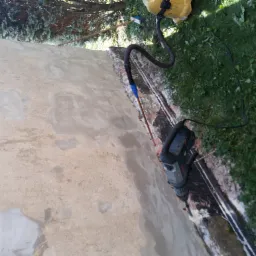 Ściana budynku w trakcie naprawy z widocznymi śladami wilgoci i naprawczymi zaprawami, obok leży wiertarka udarowa i żółty odkurzacz przemysłowy z wężem.