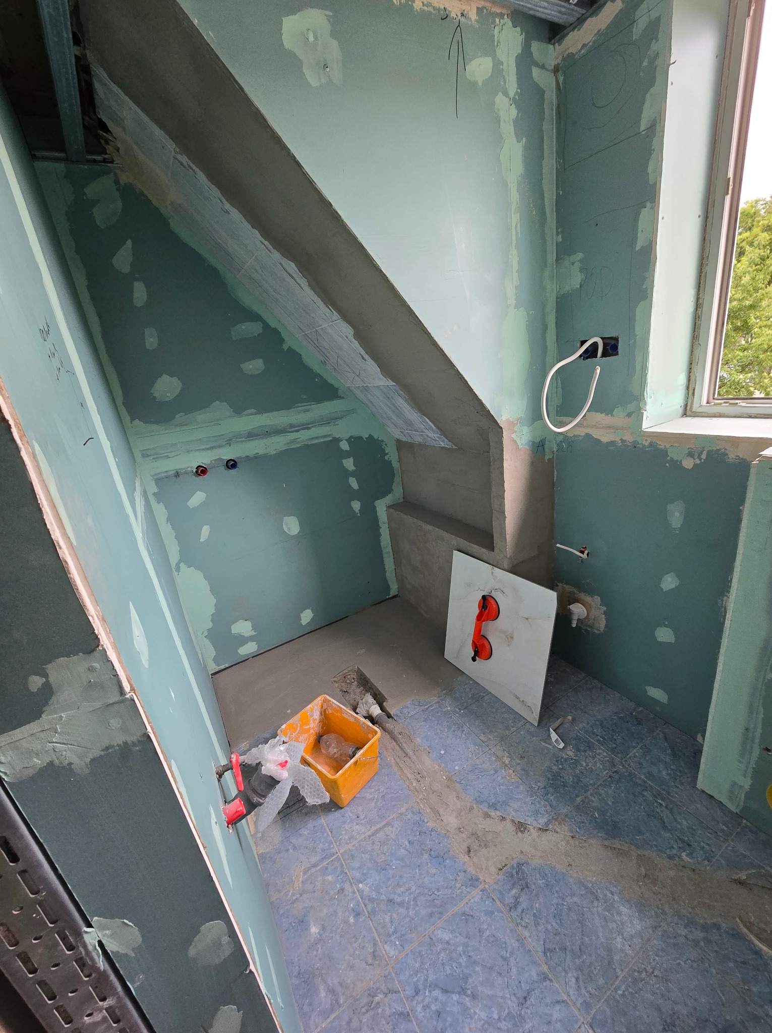 Wnętrze w trakcie prac: ściany z płyt gipsowo-kartonowych, widoczne profile, instalacje, narzędzia i płytka z przyssawkami. Prace wykończeniowe w łazience.