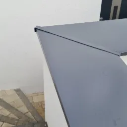 Fragment dachu z blachy na budynku, widok z góry, z widocznymi schodami wejściowymi z kostki brukowej.