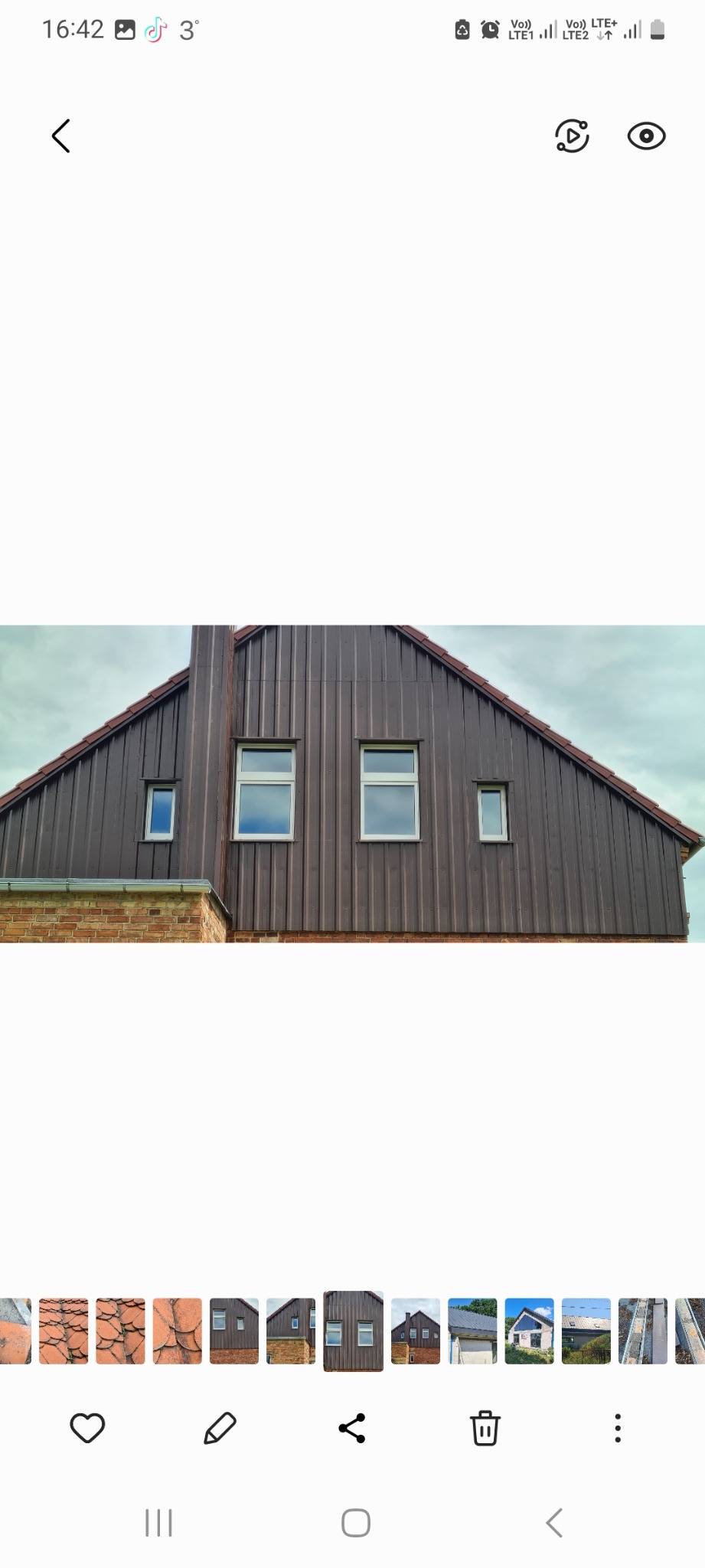 Dom z elewacją z brązowej blachy trapezowej, widoczne okna z białymi ramami i ceglana podmurówka.