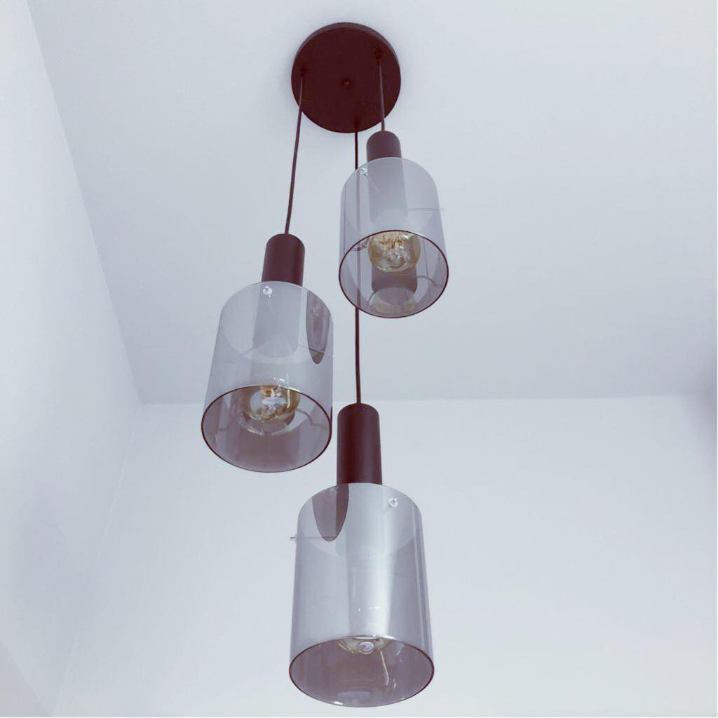 Nowoczesna lampa wisząca z trzema szklanymi kloszami w odcieniach szarości, zawieszona na czarnych przewodach i okrągłej, ciemnobrązowej podsufitce, widoczna z perspektywy żabiej z białym tłem sufitu.