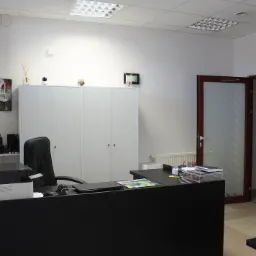 Nowoczesne wnętrze gabinetu z czarnym biurkiem, krzesłem, szafą i elementami dekoracyjnymi, takimi jak dyfuzor zapachowy, kalendarz i minimalistyczny zegar ścienny.