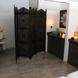 Centrum Regeneracji - gabinet masażu z elementami rehabilitacji Maciejewska Małgorzata - Jasne wnętrze gabinetu z parawanem z ciemnego drewna, stolikiem z umywalką i świecami, oraz leżanką do zabiegów z zagłówkiem.