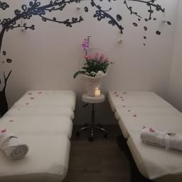Centrum Regeneracji - gabinet masażu z elementami rehabilitacji Maciejewska Małgorzata - Przygotowane stanowiska zabiegowe z białymi ręcznikami, płatkami róż i dekoracją ścienną w kształcie drzewa, oświetlone świecą na stoliku.