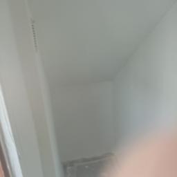 Kowalski De-lux - Świeżo pomalowany róg pomieszczenia z widoczną listwą karniszową i folią ochronną na podłodze, ujęcie z bliska z częściowo zasłoniętym obiektywem.