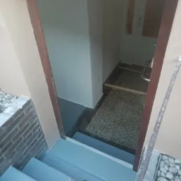 Pomieszczenie po remoncie z widocznymi pomalowanymi schodami na szaro, fragmentem ceglanej ściany i wejściem do jasnego wnętrza z widocznymi drzwiami i podłogą z lastryko.