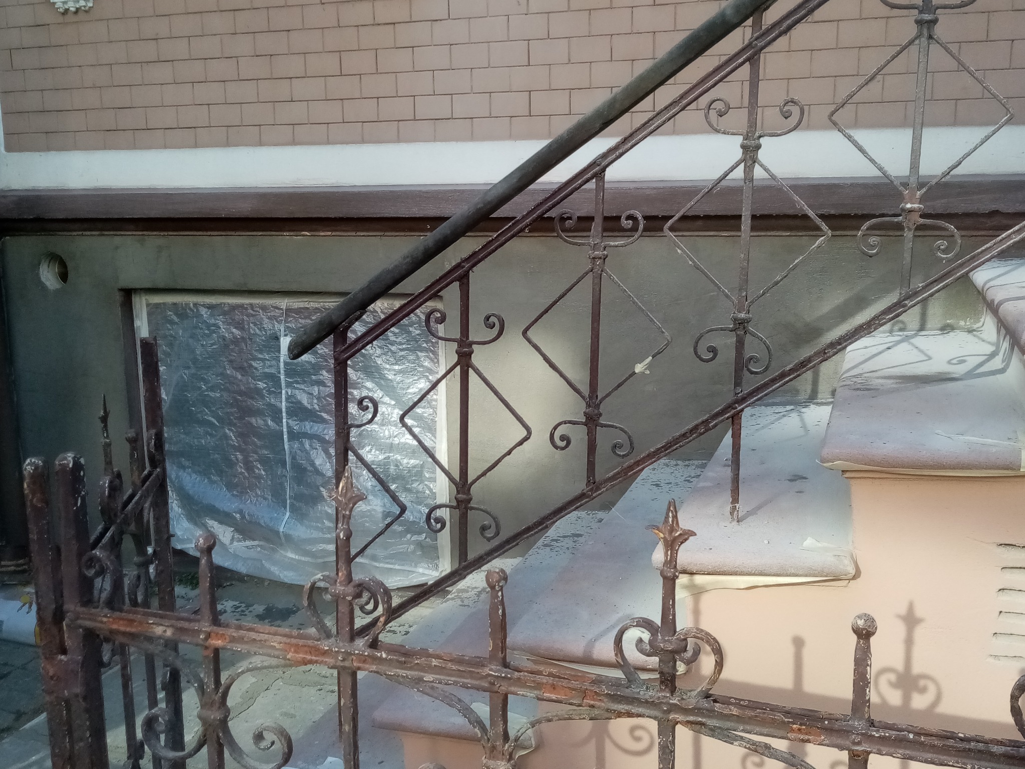 Rusty metal balustrade with decorative elements, concrete steps partially covered with dust, and a window covered with foil in the background.