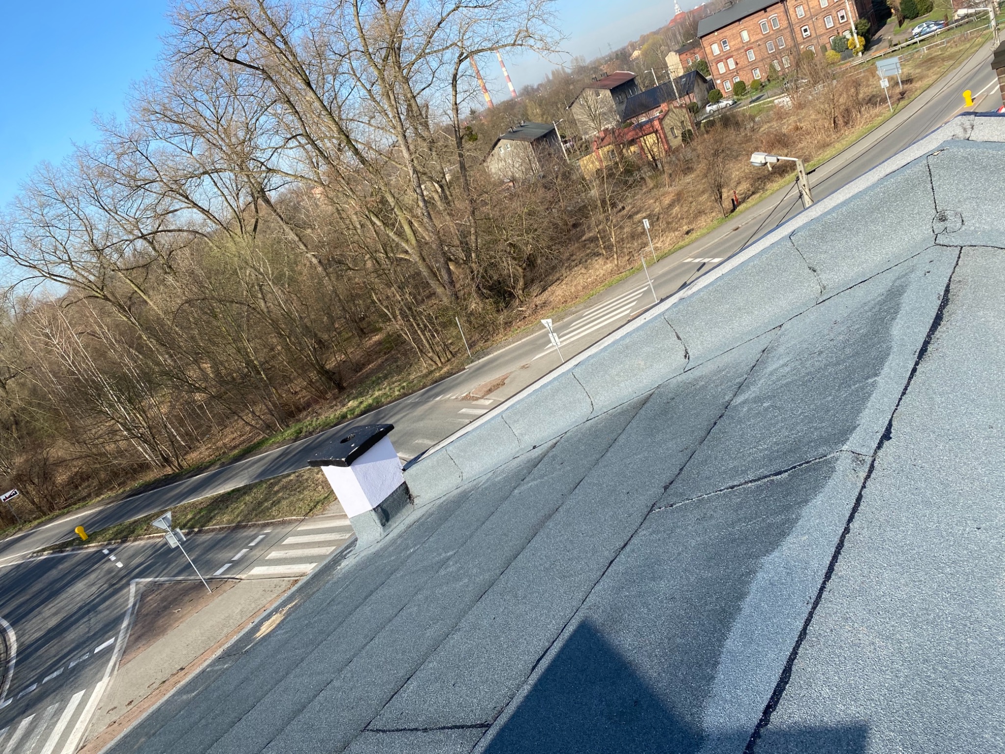 Nowe pokrycie dachowe z papy termozgrzewalnej w kolorze szarym, widok z góry na komin i okoliczną zabudowę miejską.