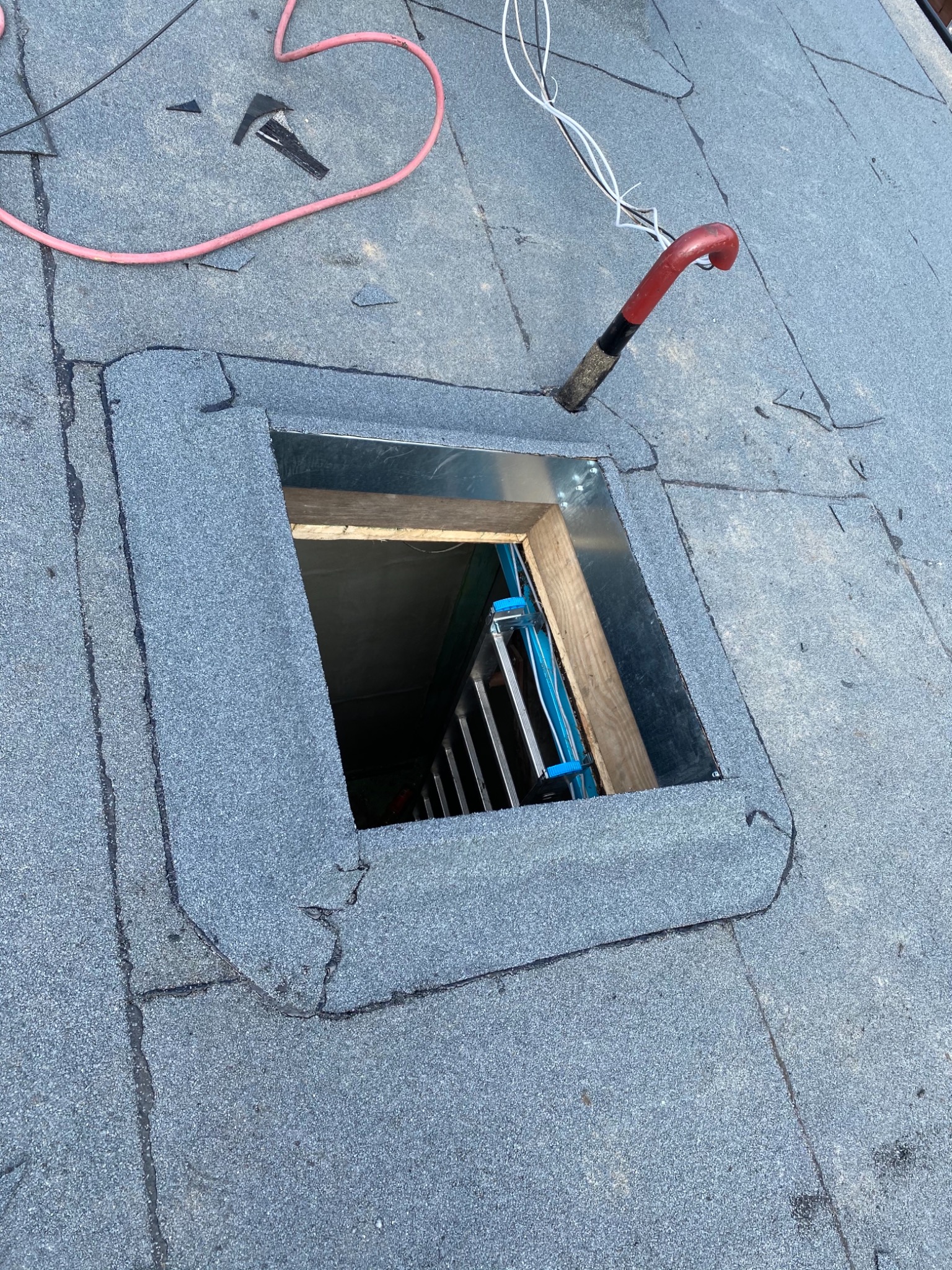 Otwór w pokryciu dachowym z widoczną drabiną wewnątrz, narzędzia dekarskie i przewody na dachu.