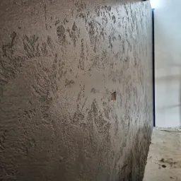 Szara ściana z efektem dekoracyjnym w Rybniku, widoczna puszka elektryczna i fragment sufitu z niebieskim zabezpieczeniem.