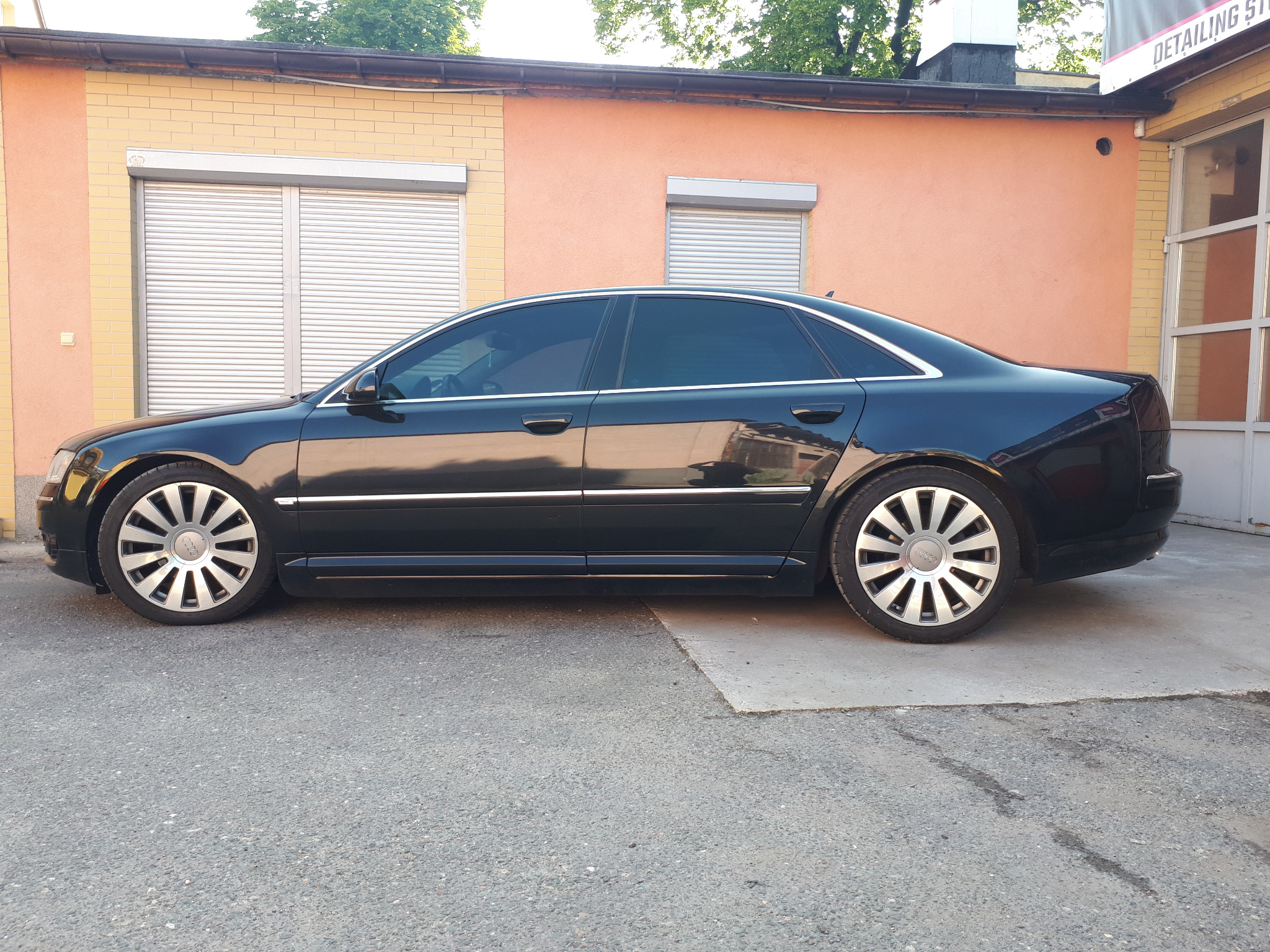 Czarny samochód Audi A8 po przyciemnieniu szyb, zaparkowany przed budynkiem z roletami zewnętrznymi.