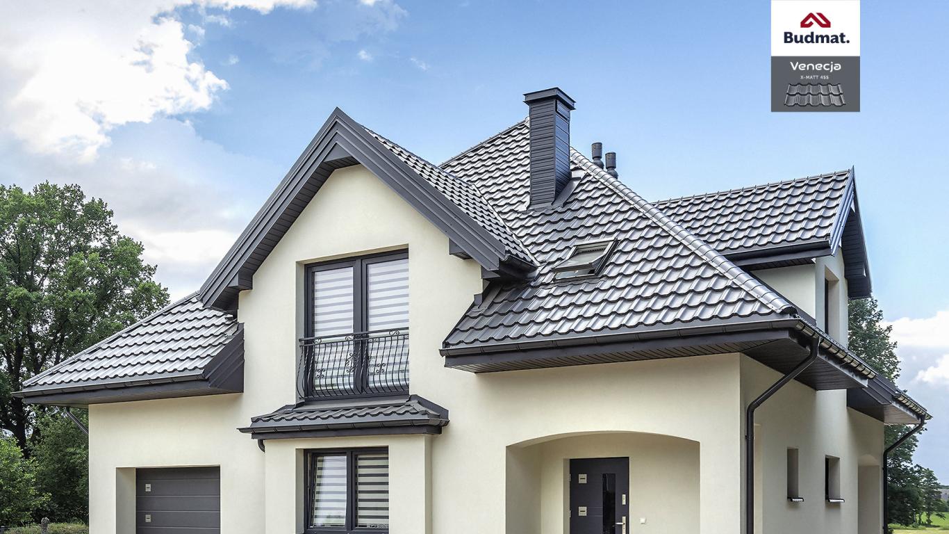 Dom jednorodzinny z szarą dachówką karpiówką, ciemnymi rynnami i kominem, widoczny znak producenta Budmat.