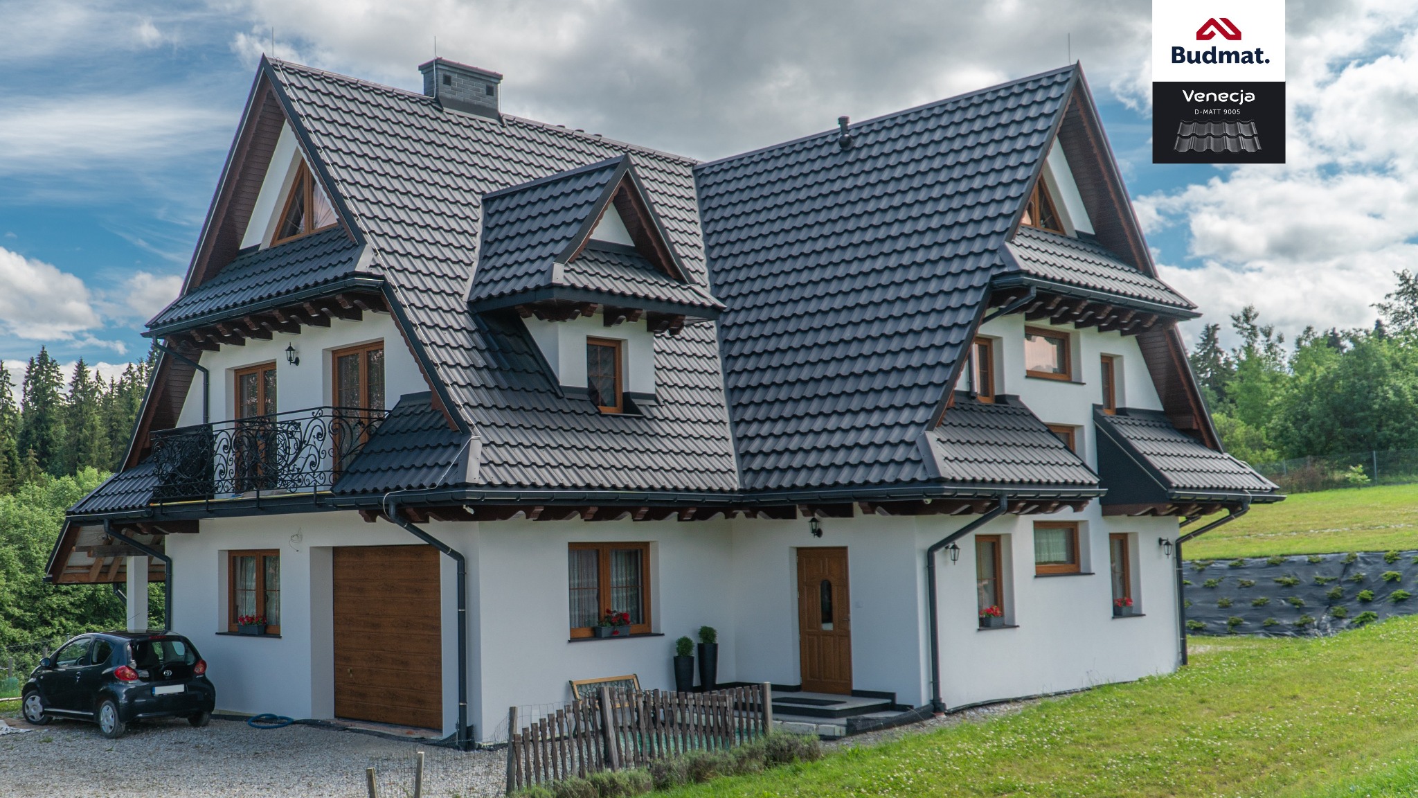 Nowoczesny dom jednorodzinny z ciemnoszarą dachówką karpiówką, drewnianymi oknami, czarnymi rynnami i logo producenta na górze po prawej stronie. Na podjeździe stoi czarny samochód.