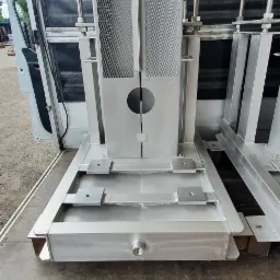 Metalowa konstrukcja z kratownicą i otworem, prawdopodobnie element większej maszyny, transportowana wewnątrz furgonetki.