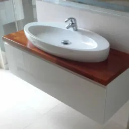 Nowoczesna łazienka z owalną umywalką nablatową na blacie z ciemnego drewna, szafka pod umywalką w białym połysku.