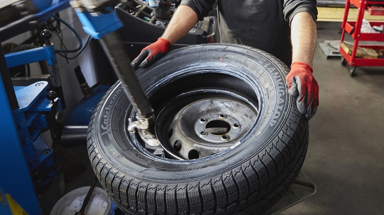 Opona zimowa LAND NAVIGATOR na feldze stalowej podczas montażu na maszynie w warsztacie, ręce w czerwonych rękawicach ochronnych trzymają oponę, widoczny fragment maszyny do montażu opon.