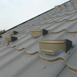 Szary dach z blachodachówki z zamontowanymi metalowymi uchwytami, widok z dołu pod kątem.