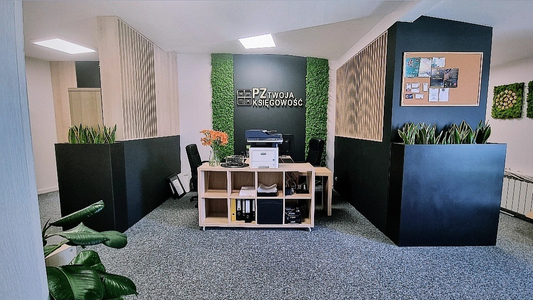 Nowoczesne biuro rachunkowe z recepcją, ścianą z mchu i logo firmy PZ Twoja Księgowość, drewnianym regałem z segregatorami i drukarką, donicami z roślinami, tablicą korkową i szarym dywanem...