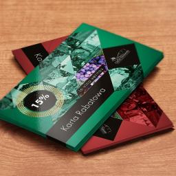 PIXGOBLIN Paweł Pożoga - Dwa błyszczące, kolorowe vouchery rabatowe na drewnianym stole. Zielony voucher na wierzchu z napisem 'Karta Rabatowa' i logo wina, czerwony voucher częściowo widoczny pod spodem.