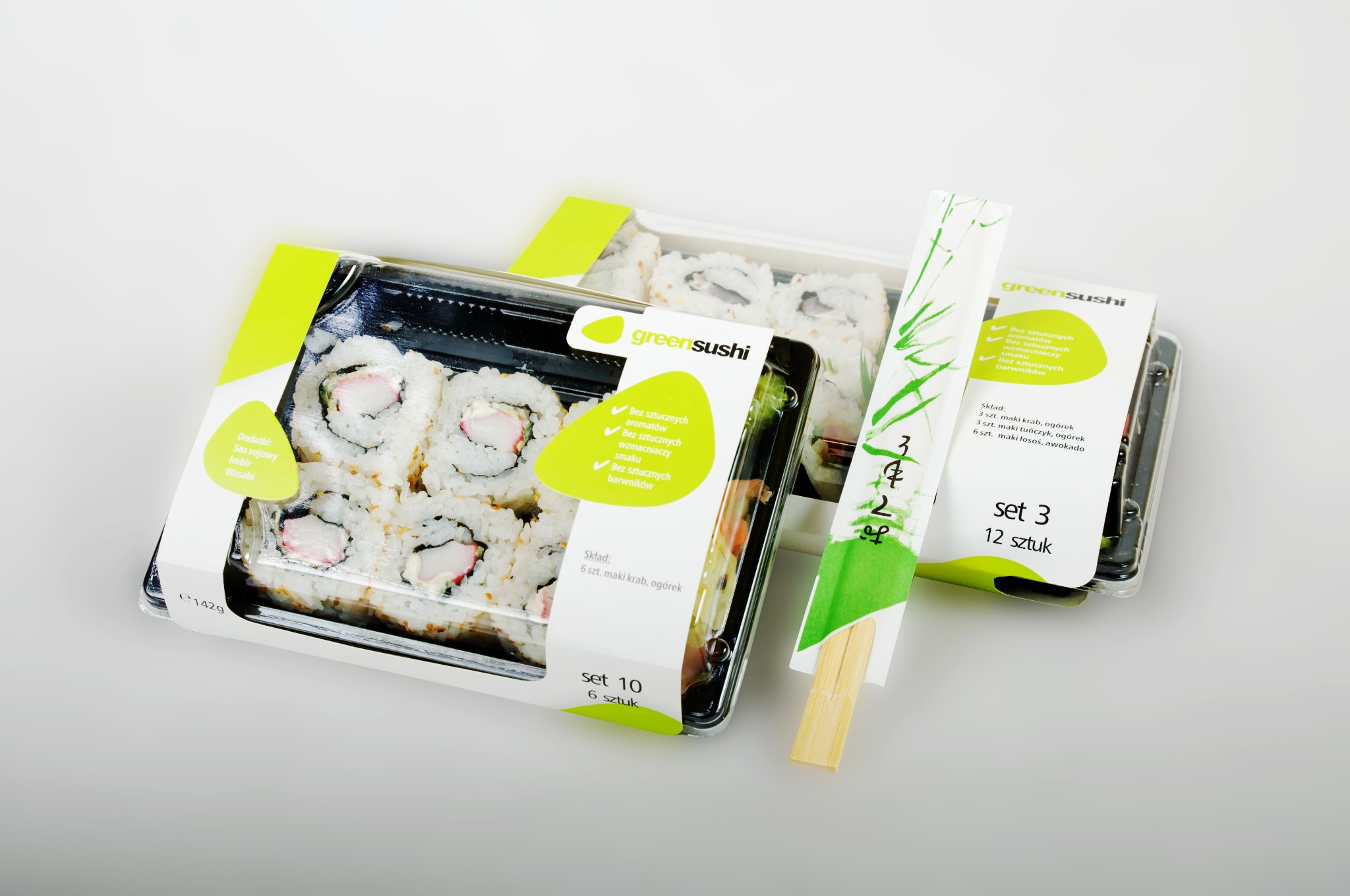 Zestawy sushi w plastikowych opakowaniach z zielonymi akcentami, etykietami informacyjnymi i pałeczkami, ułożone na jasnym tle.