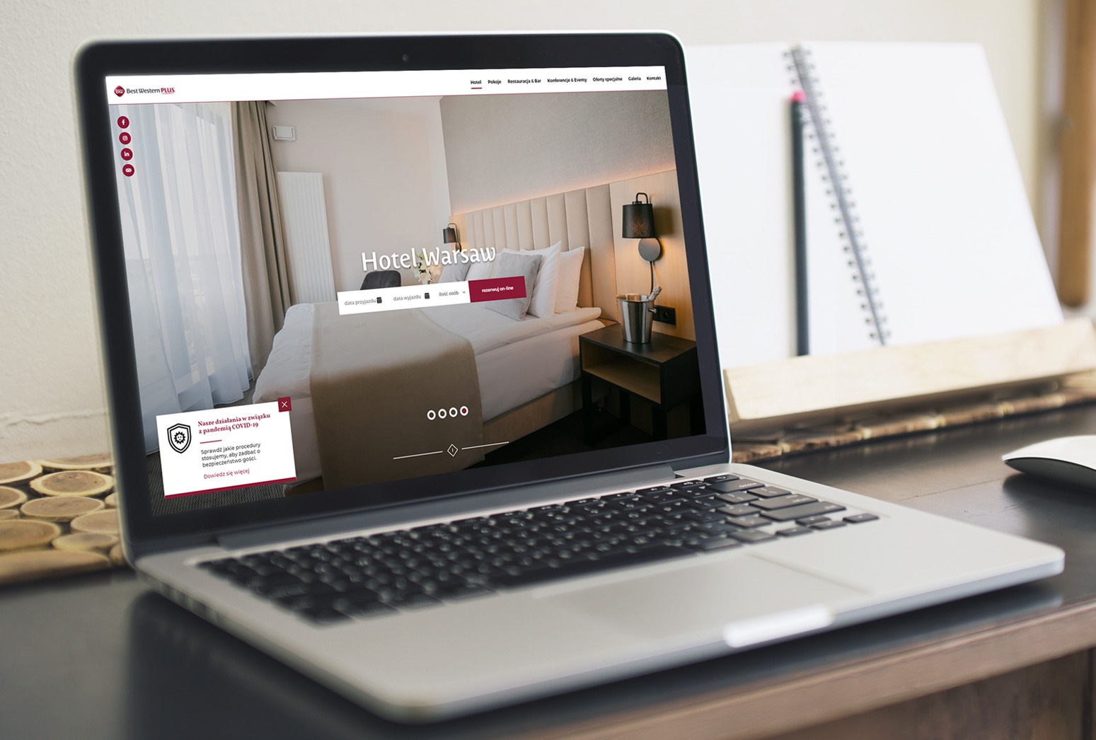 Laptop wyświetlający stronę internetową hotelu Best Western PLUS Warsaw z widokiem pokoju, obok notatnik z ołówkiem i myszka.