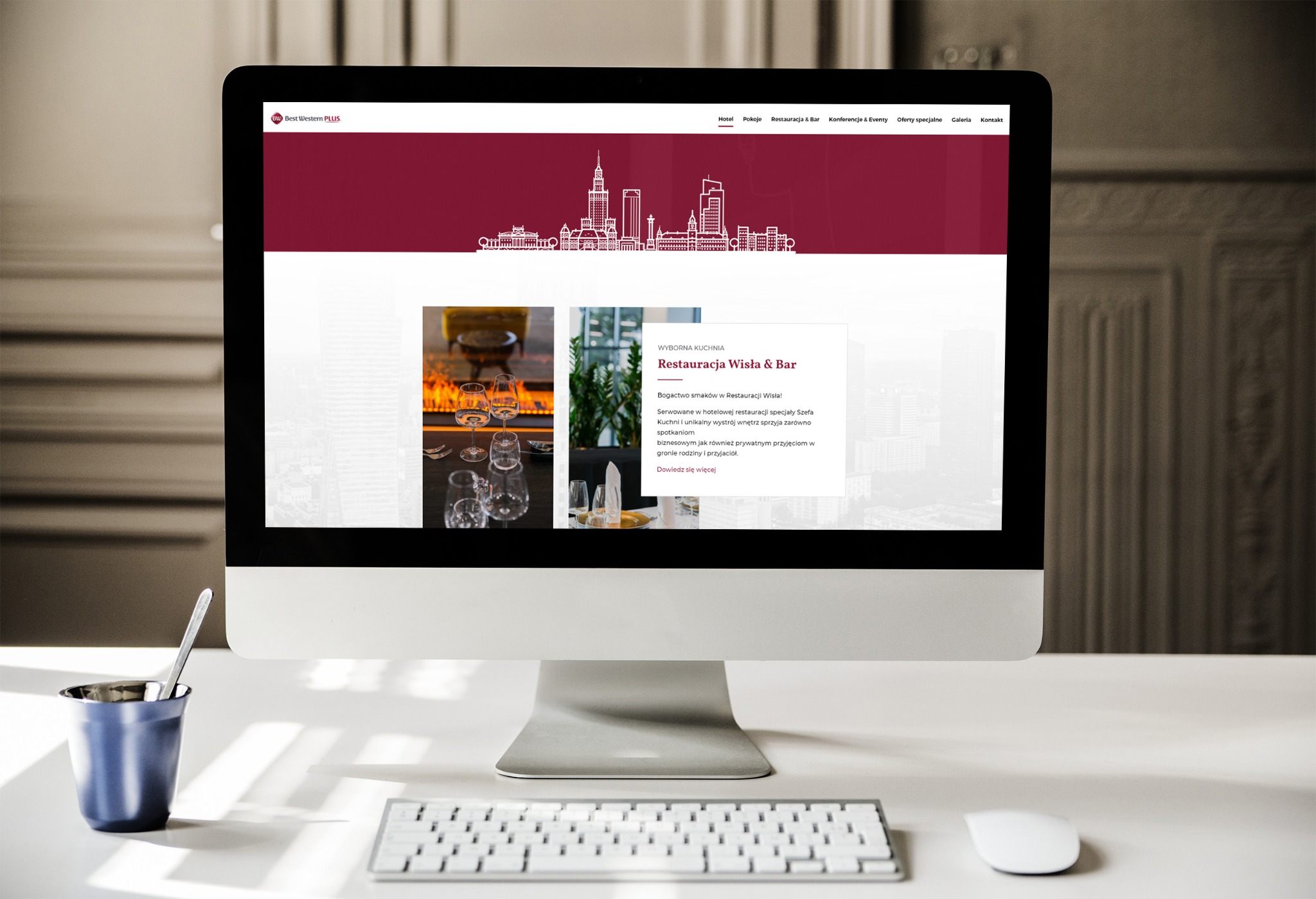Ekran komputera iMac wyświetlający stronę internetową hotelu Best Western Plus z widokiem na panoramę Warszawy i ofertą restauracji Wisła & Bar, obok na biurku kubek z łyżeczką i klawiatura Apple.