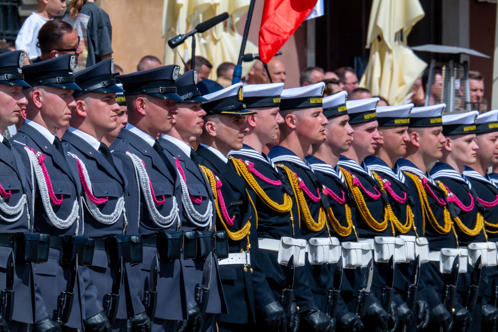 Uroczysty pochód żołnierzy w mundurach galowych Marynarki Wojennej i Wojska Polskiego na Placu Zamkowym w Warszawie podczas obchodów 3 Maja, z widocznymi detalami umundurowania i bronią.