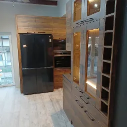 Nowoczesna kuchnia z drewnianymi szafkami, czarną lodówką side-by-side i oświetleniem LED wewnątrz witryn, widok na okno z widokiem na zewnątrz.