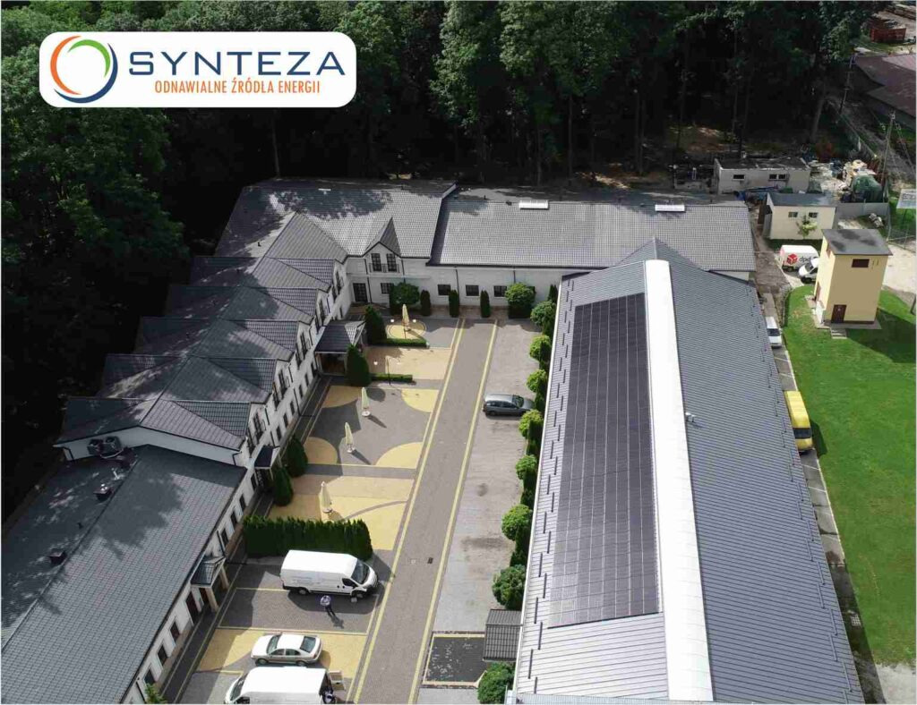 Widok z lotu ptaka na budynek z panelami słonecznymi na dachu, logo firmy Synteza widoczne w lewym górnym rogu.