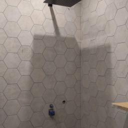 SAMSARA Marcin Majewski - Łazienka w trakcie wykańczania w Banino: montaż podtynkowej instalacji prysznicowej z deszczownicą na ścianie wyłożonej szarymi płytkami hexagonalnymi. Widoczne przyłącza wodne i fragment...