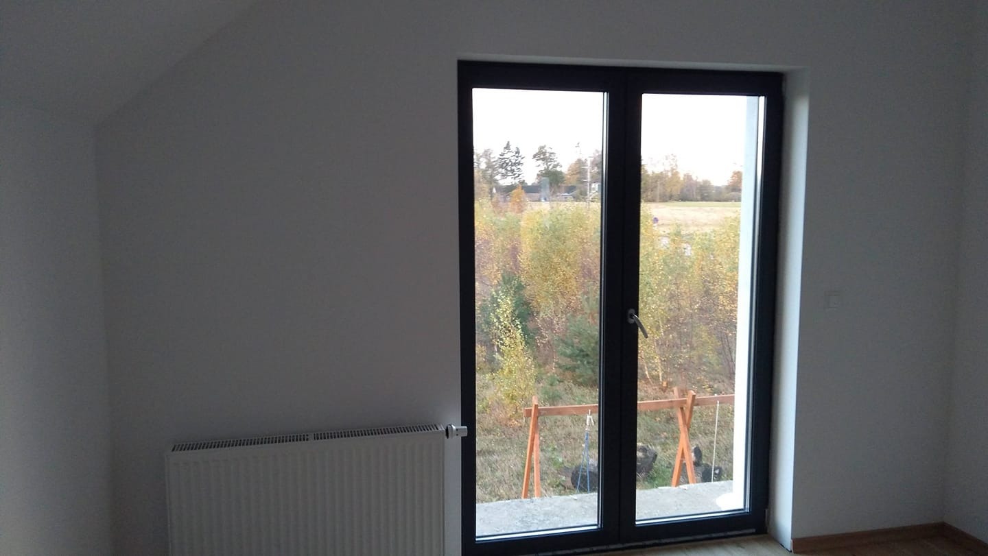 Pusty pokój po remoncie z grzejnikiem, widok z okna balkonowego na jesienny krajobraz i huśtawkę.