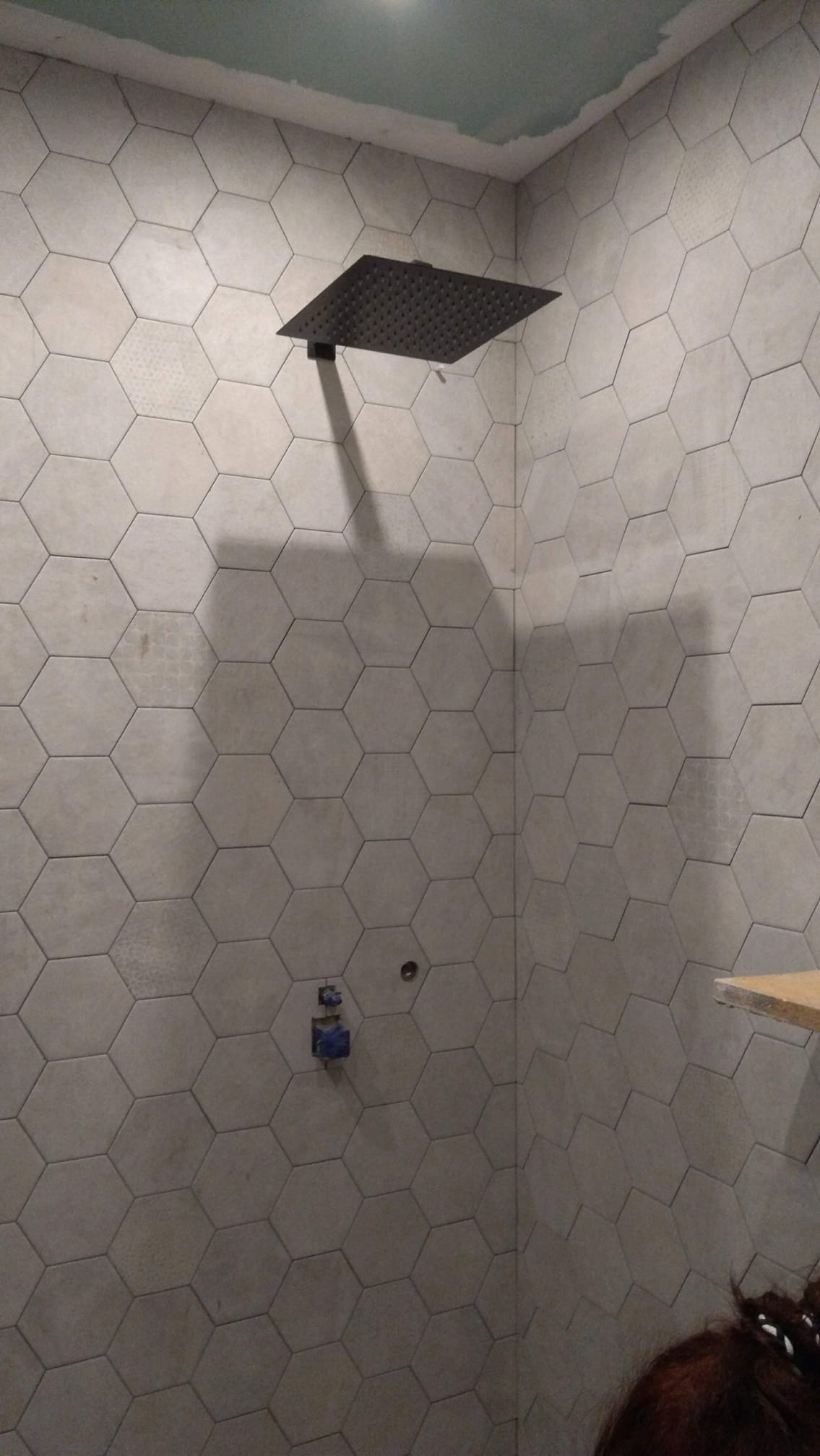 Łazienka w trakcie wykańczania w Banino: montaż podtynkowej instalacji prysznicowej z deszczownicą na ścianie wyłożonej szarymi płytkami hexagonalnymi. Widoczne przyłącza wodne i fragment...