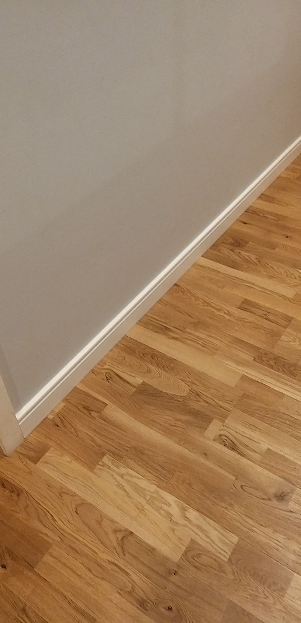 Fragment korytarza po remoncie: parkiet dębowy ułożony w jodełkę, biała listwa przypodłogowa MDF, szara ściana z białą listwą wykończeniową przy podłodze.