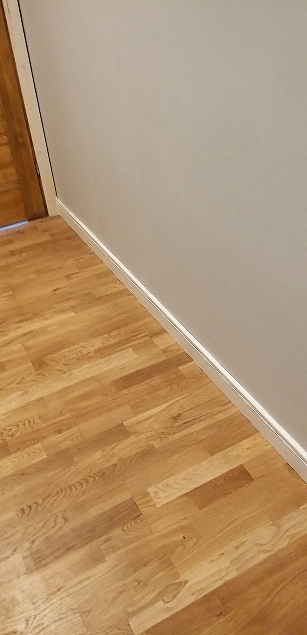 Korytarz po remoncie: deski dębowe na podłodze ułożone diagonalnie, białe listwy przypodłogowe MDF, gładź na ścianach pomalowana na jasny szary kolor, widoczny fragment drewnianych drzwi z białą...