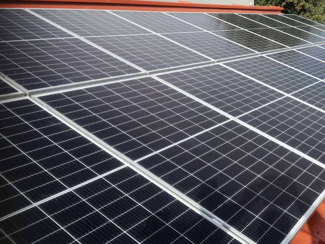 Panele słoneczne na dachu z czerwoną dachówką, widoczne z boku pod kątem.