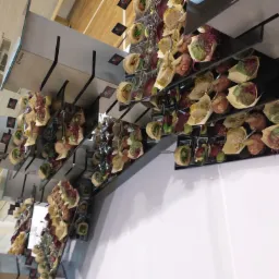 Nowoczesna prezentacja różnorodnych przekąsek cateringowych na metalowych półkach z czarnymi akcentami, widoczne logo firmy na etykietach.