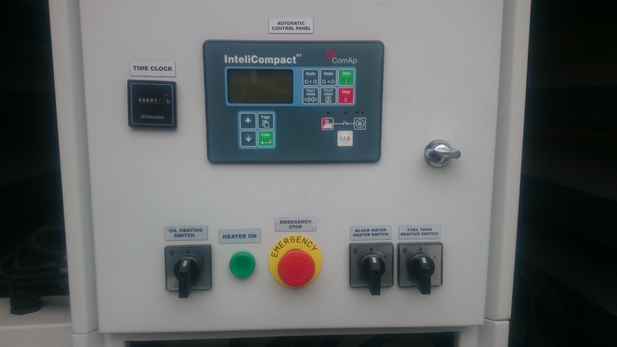 Panel sterowania agregatu prądotwórczego z wyświetlaczem IntelliCompact, przyciskiem awaryjnego zatrzymania, włącznikami i licznikiem czasu pracy.