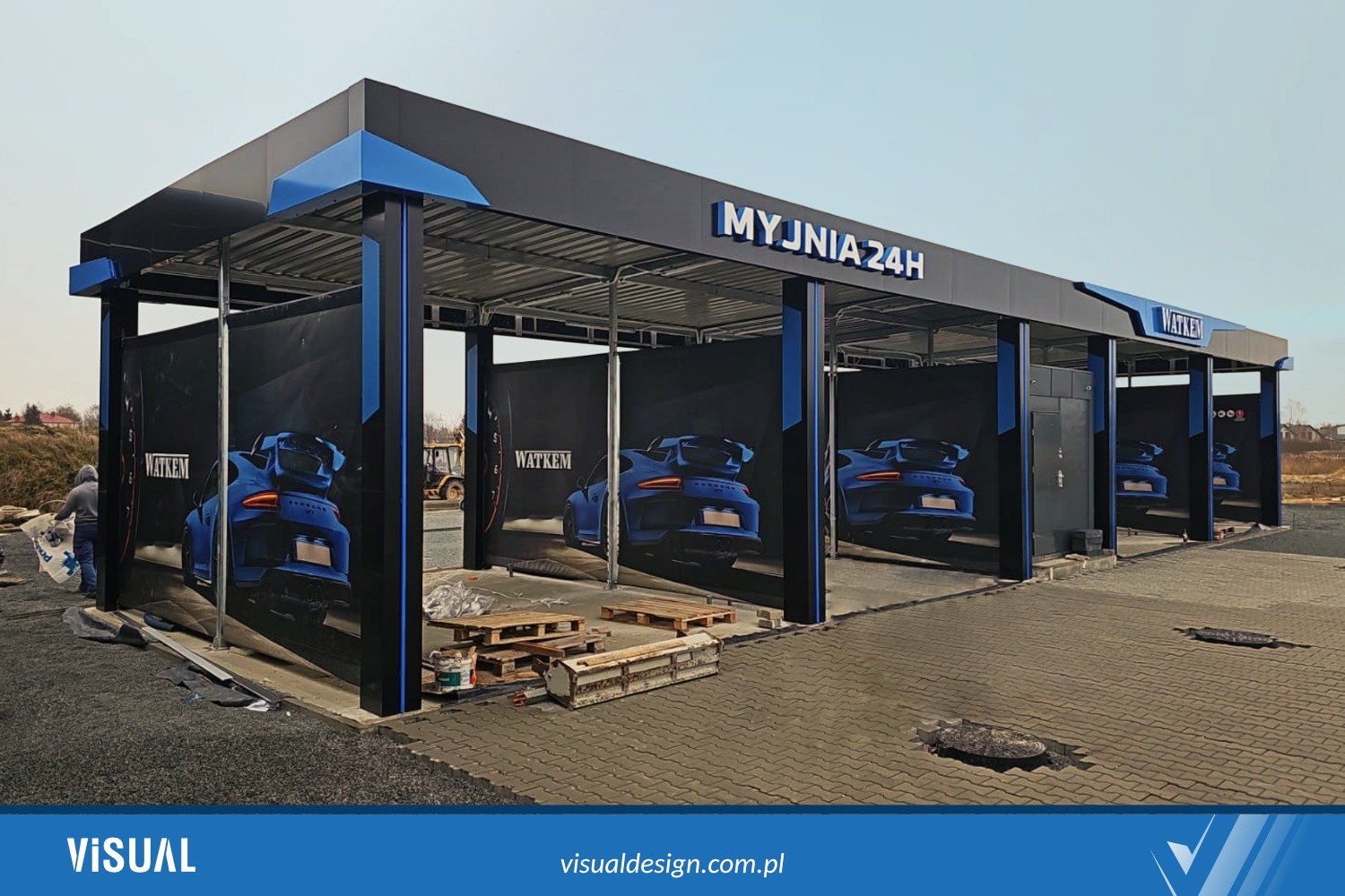 Nowoczesna, samoobsługowa myjnia 24h z czarną konstrukcją i niebieskimi akcentami, ozdobiona grafiką z motywem sportowego samochodu WATKEM.
