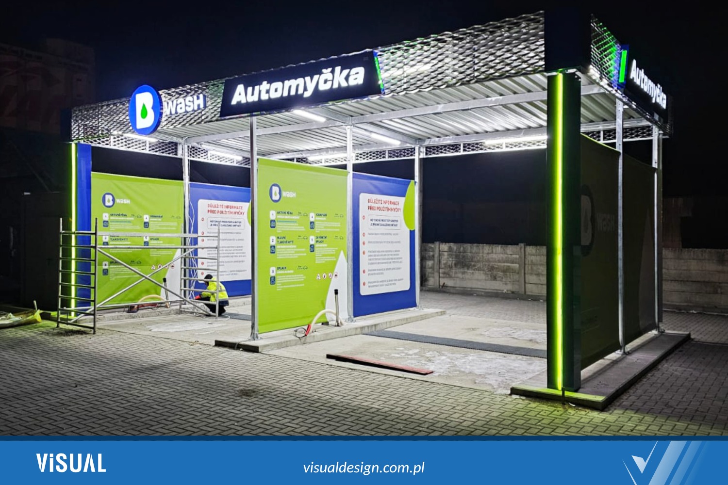 Nowoczesna konstrukcja myjni samochodowej z logo 'B Wash' w Ostrowcu Świętokrzyskim, oświetlona ledami. Widoczny pracownik w odblaskowej kamizelce.