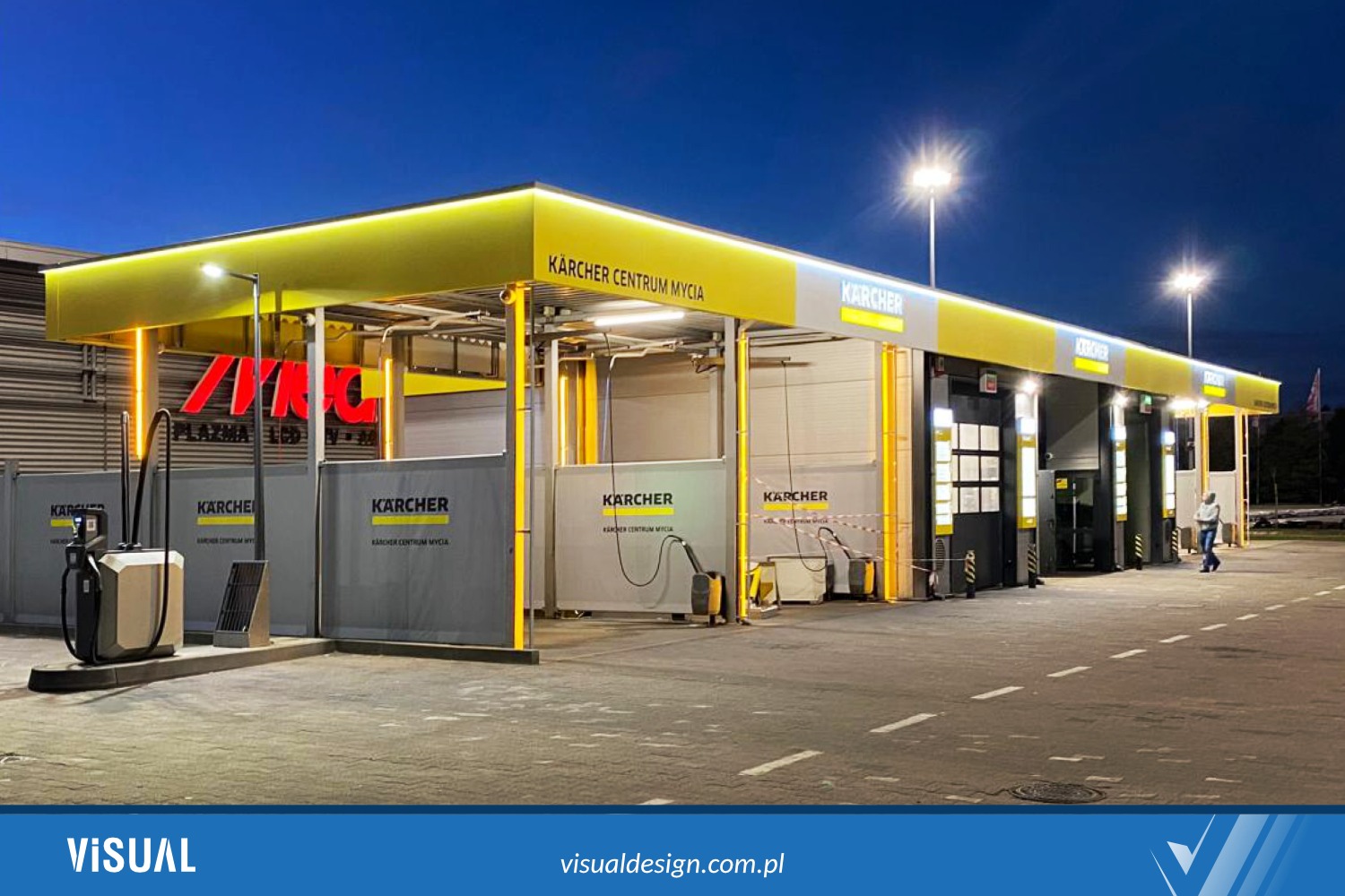 Nowoczesna, żółto-szara stacja mycia Kärcher Centrum Mycia oświetlona wieczornym światłem. Widoczny automat do mycia i osoba przechodząca obok stanowisk.